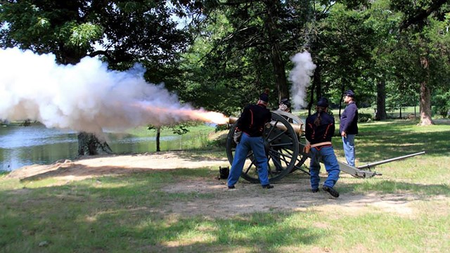 People in military garb fire a canon. 